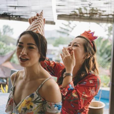 atvira akimirka, kai azijietė kinė padeda seseriai užsirišti vakarėlio kepurę besiruošianti gimtadienio šventei