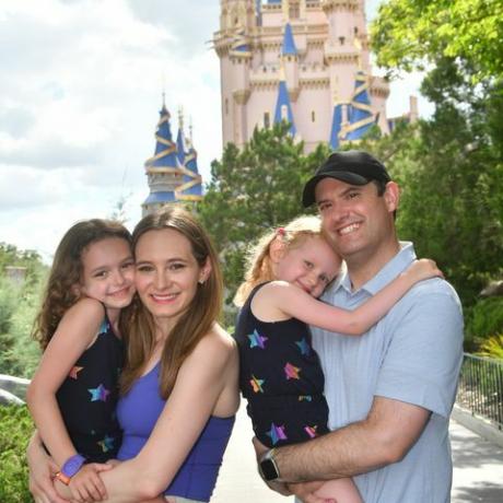 šeima šypsosi priešais Pelenės pilį magijos karalystės parke