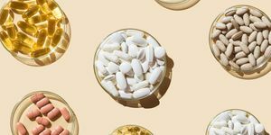 įvairios tabletės ir kapsulės, vitaminai ir maisto papildai Petri lėkštelėse smėlio spalvos fone